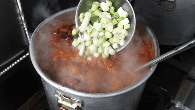 Spicy Chinese broth boiling in pot with green onions