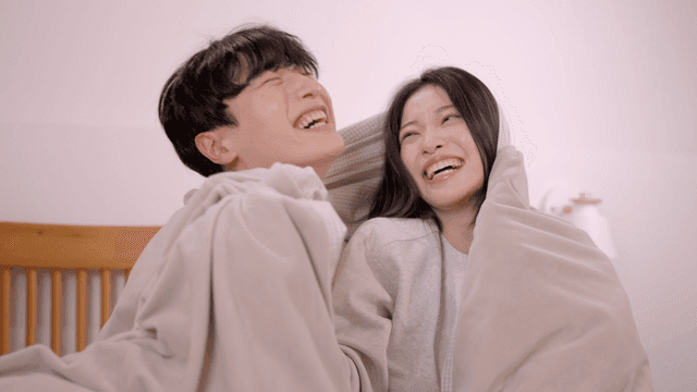 Smiling couple relaxing under blanket in bedroom