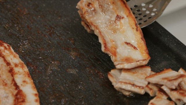 Cutting sizzling pork belly in a hot pan with scissors