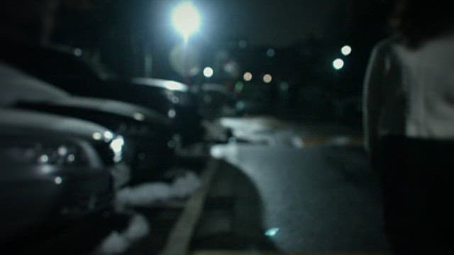 Man Watching Woman Walking throughi Urban Parking Lot at Night