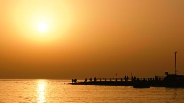 Sunset over a pier with people gathered and serene sea