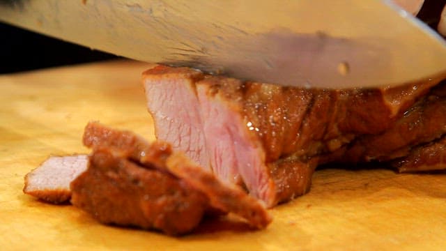 Slicing juicy cooked boiled pork on a board