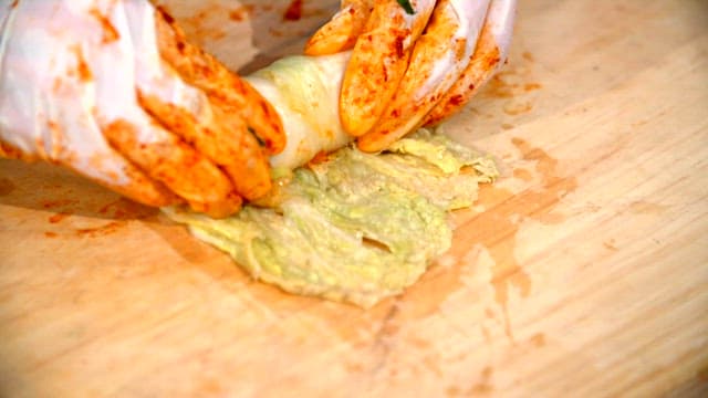 Hands rolling kimchi on a wooden board