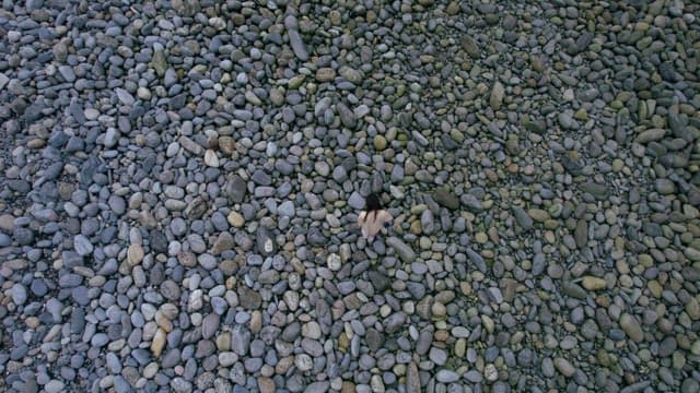 Person Walking Alone on a Land Covered with Many Pebbles