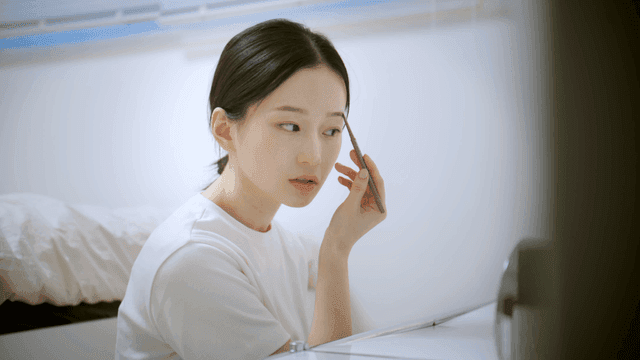 Woman applying eyebrow makeup in bright room