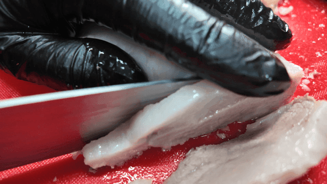 Slicing boiled pork on a red cutting board