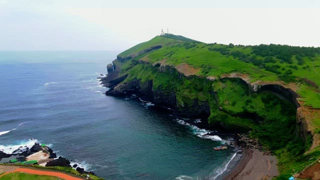 Coastal cliffs with green hills and a lighthouse