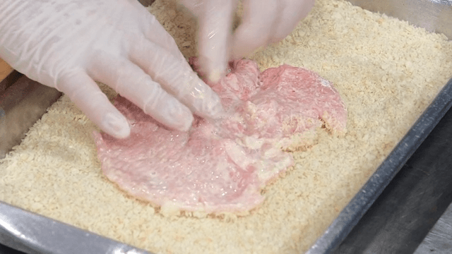 손으로 생돼지를 빵가루에 입히는 모습