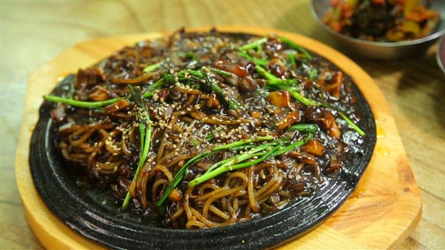 Seafood Jjajang noodles on an iron plate with steaming hot sauce