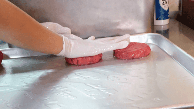 Gloved hands shaping raw meat patties