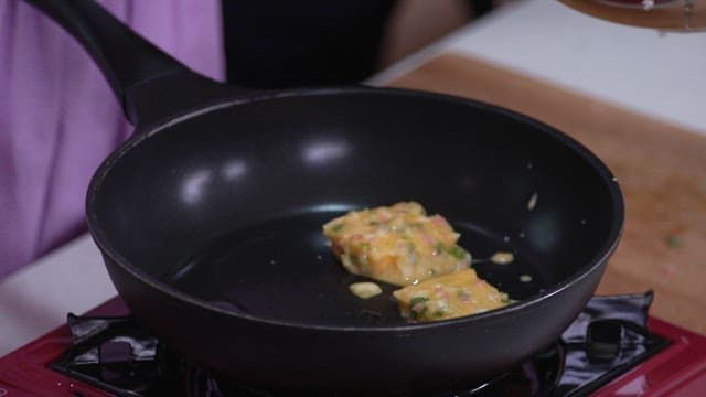 Cooking slices of bread coated with green onion and egg mixture in a frying pan