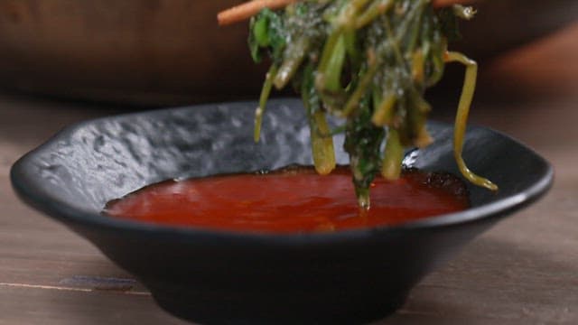 Dipping slightly blanched water parsley into soy sauce with chopsticks