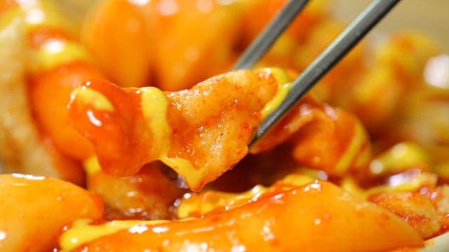 Chopstickful of spicy tteokbokki with mustard sauce