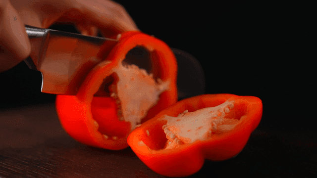 Red bell pepper being sliced on a board