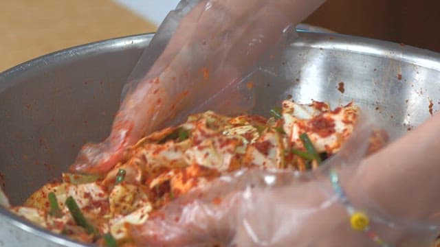 장갑을 끼고 금속 그릇에서 양배추 겉절이를 버무리는 사람