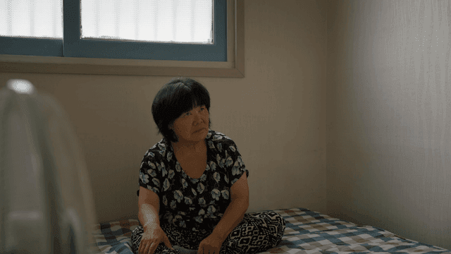 실내에서 침대에 앉아 있는 노인 여성