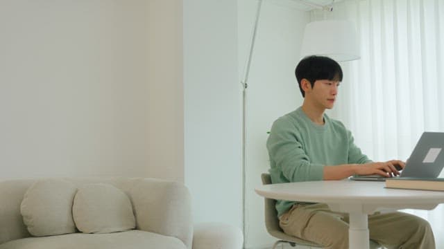 Man using laptop at living room table in bright interior