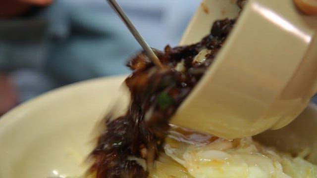 Pouring the thick black bean sauce over the noodles with the fried egg on top