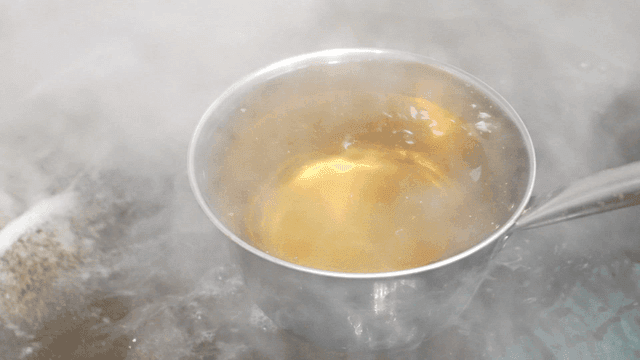 Ladle scooping out boiling broth from large pot