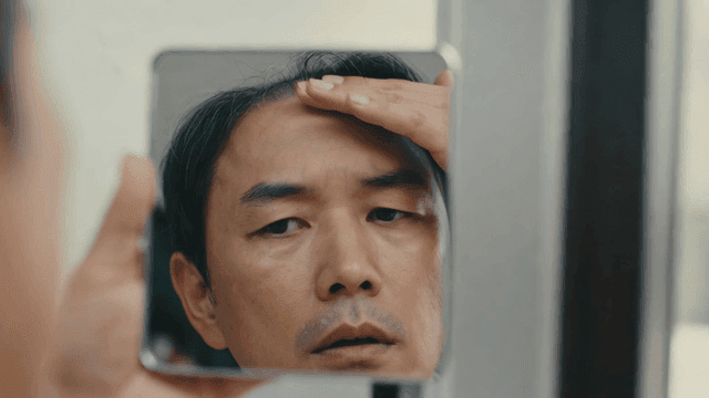 Middle-aged man checking his hair loss in mirror