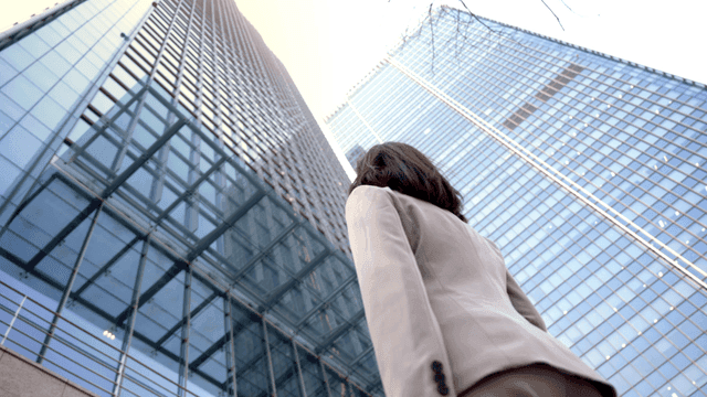 Back view of female office worker looking up at high-rise building