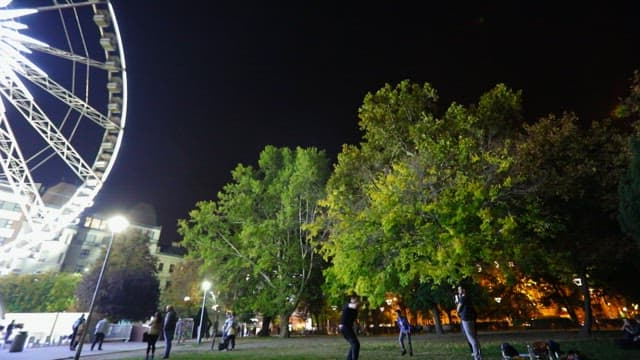 People enjoying the night in city park with illuminated ferris wheel