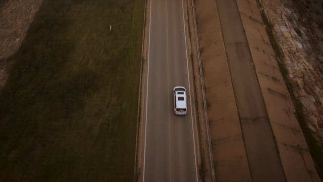 Car driving on a coastal road surrounded by greenery and the sea at sunset