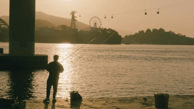 People fishing on riverbank at sunset and cable car