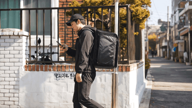 휴대폰을 보며 거리를 걷는 배달원
