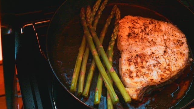 프라이팬에서 아스파라거스와 구운 생선을 요리하는 모습