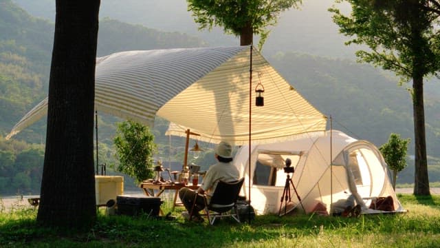 Resting under a tent on the grass decorated with camping equipments