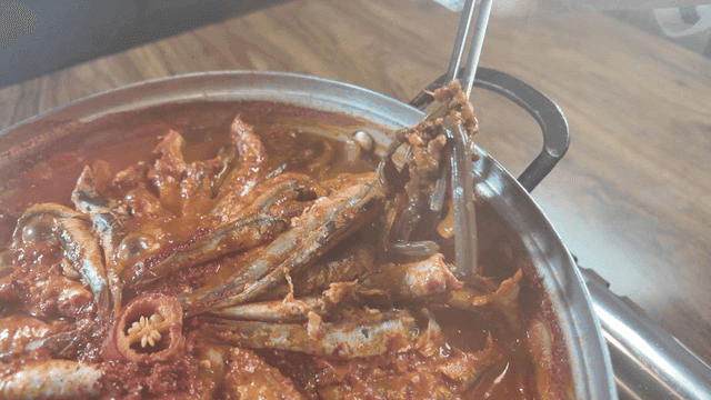 Chopsticks picking up bracken from spicy anchovy stew boiling in pot