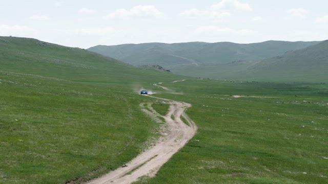 Blue car driving on a dirt road in a green valley