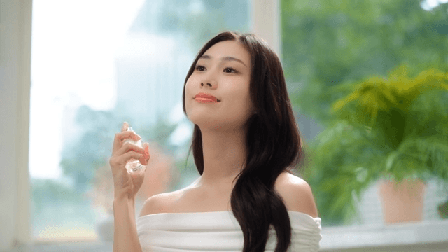 미소를 지으며 실내에서 향수를 뿌리는 여성