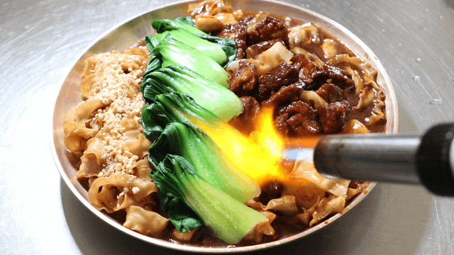 Torch searing beef stir-fried noodles topped with bok choy