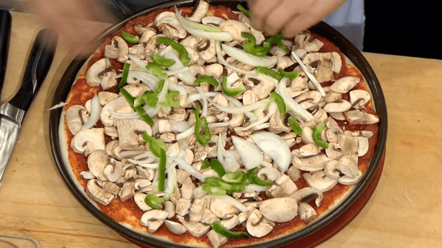 토마토 소스가 발린 피자 도우 위에 각종 재료를 올리는 손