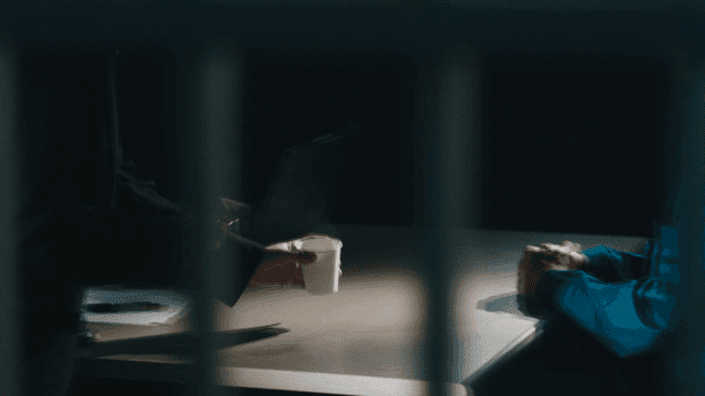 Detective hands coffee to suspect in dark room.