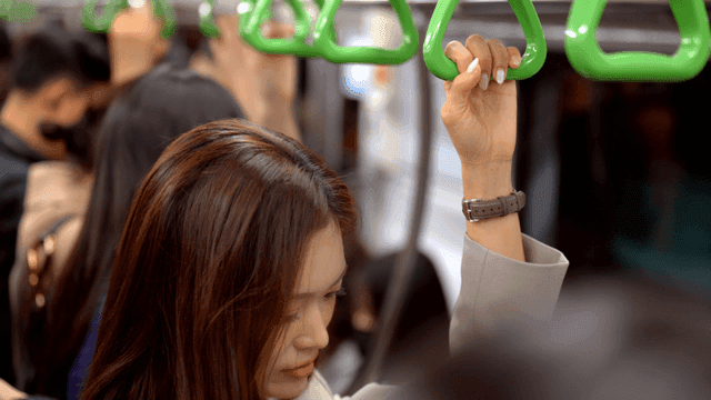 Woman standing holding handrail in crowded subway