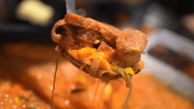 Ladle scooping sausage-filled budaejjigae