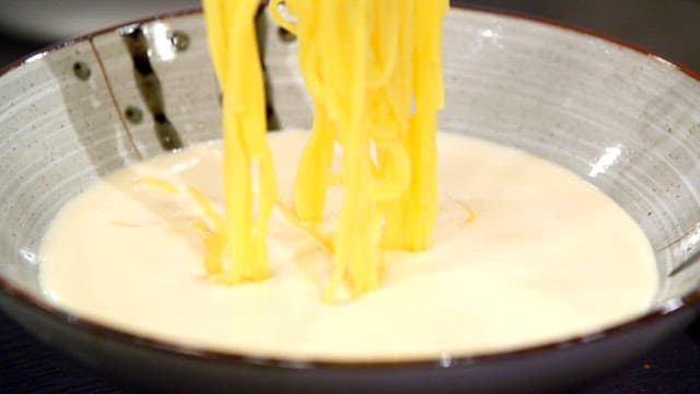 Yellow noodles being put in soybean soup