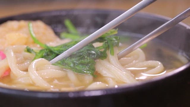 Chopstickful of udon noodles with vegetables and fish cake