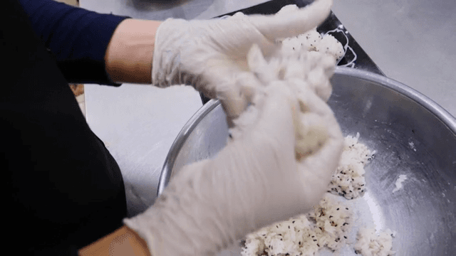 Gloved hands shaping rice balls in a bowl