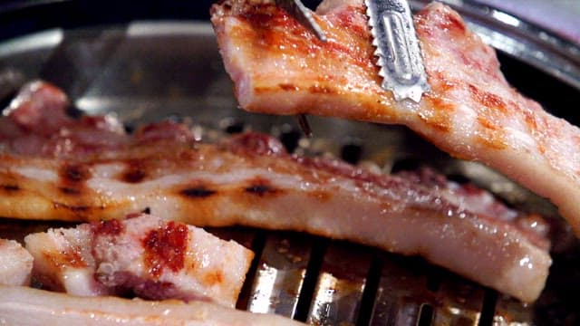 Grilled pork belly being cut with scissors