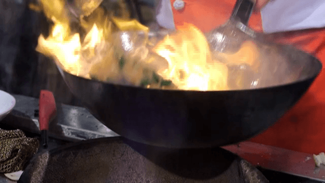 Chef cooking with a wok over hot fire