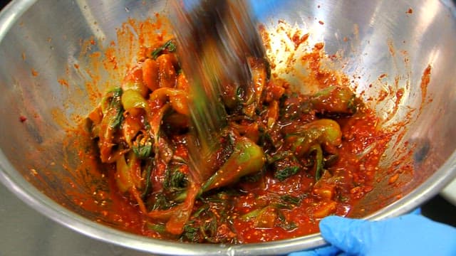 Mixing bok choy kimchi in a large metal bowl