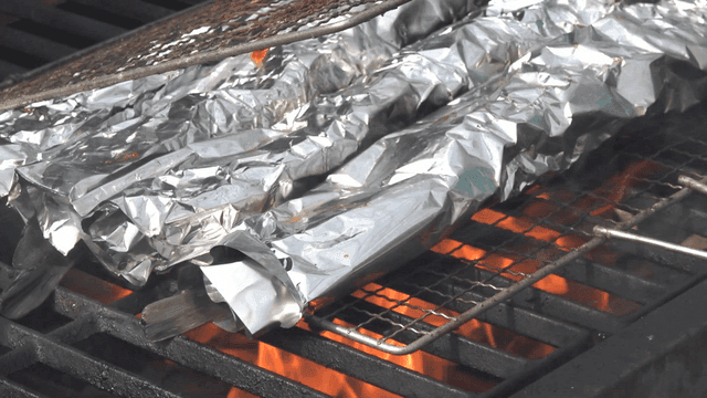 Grilling foil-wrapped fish over flame
