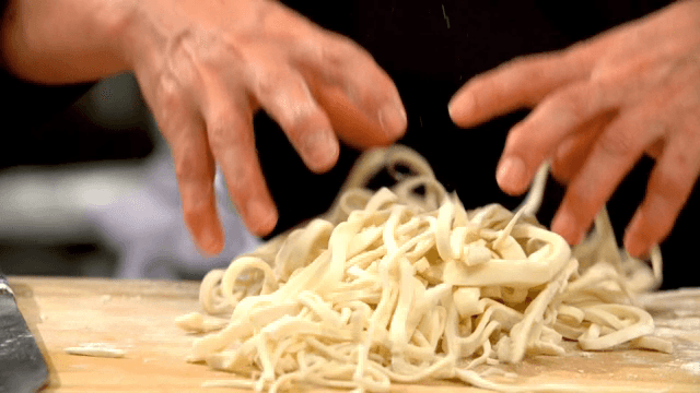 Hands untangling clumped noodles