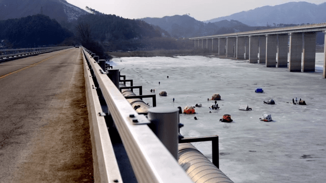 다리 아래 얼어붙은 호수에서 얼음 낚시하는 사람들