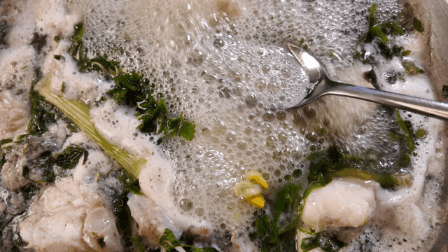 Spoon scooping up boiling anglerfish stew with vegetables