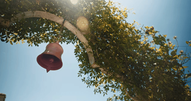 잎이 무성한 아치 아래 매달린 종